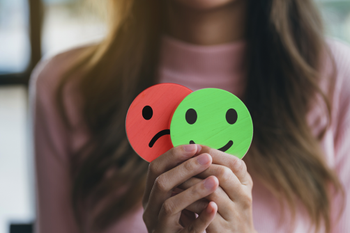 woman holding a smiley face in front of a red frowny face