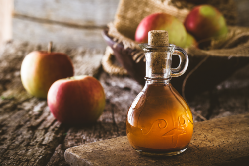 Container of apple cider vinegar with apples in the background